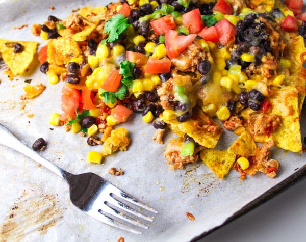 Loaded Chicken Nachos with a fork on a sheet pan