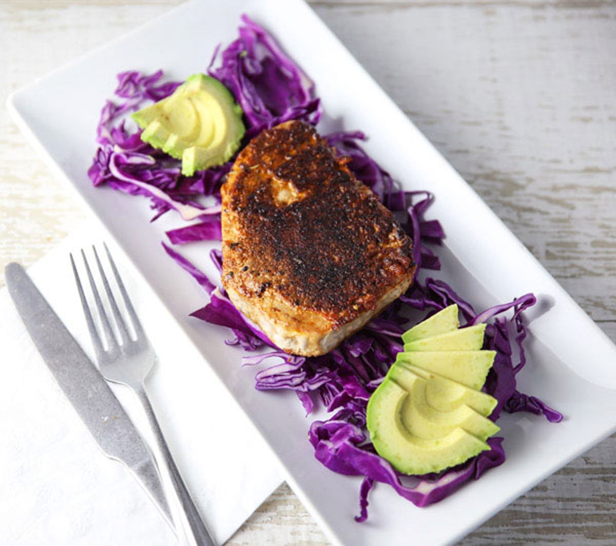 blackened tuna steak on a plate with cabbage and avocado