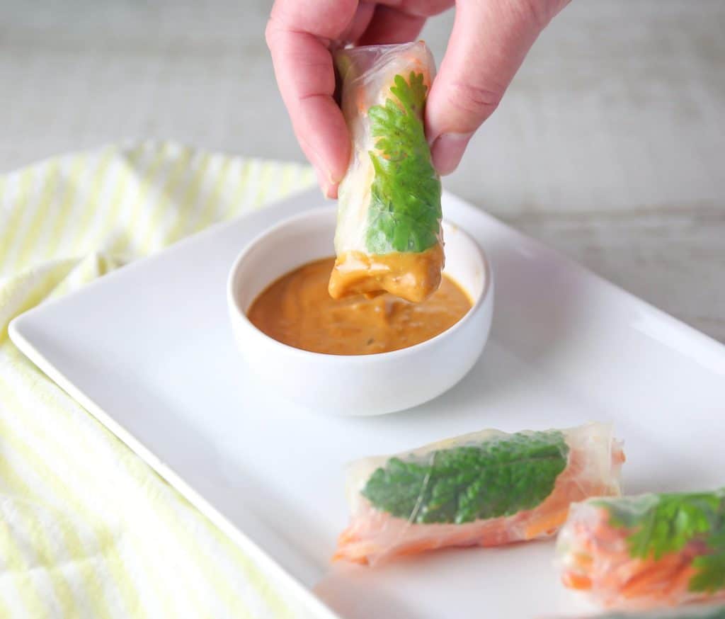 dipping a veggie spring rolls into spicy peanut sauce