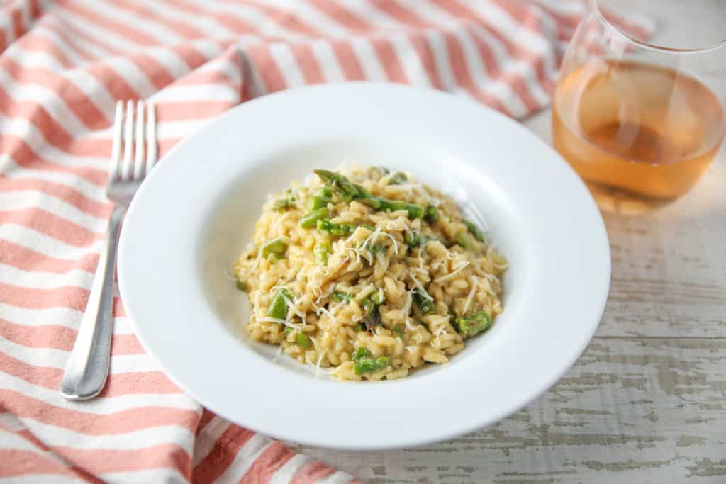 lemon asparagus risotto in a bowl with a glass of wine