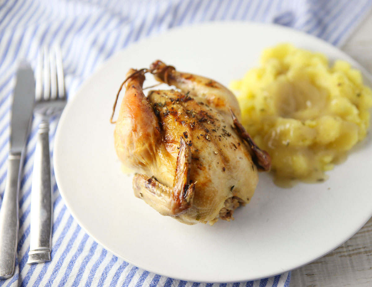 Cornish game hen on a plate with potatoes