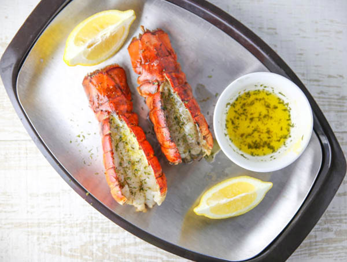 grilled lobster tails on a platter with butter and lemon